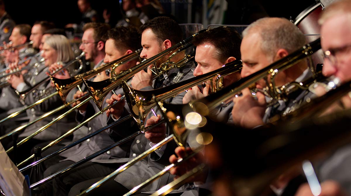 Reihe von Posaunisten in einem Orchester oder Blasorchester während eines Konzerts – Fokus auf das Zusammenspiel der Musiker.